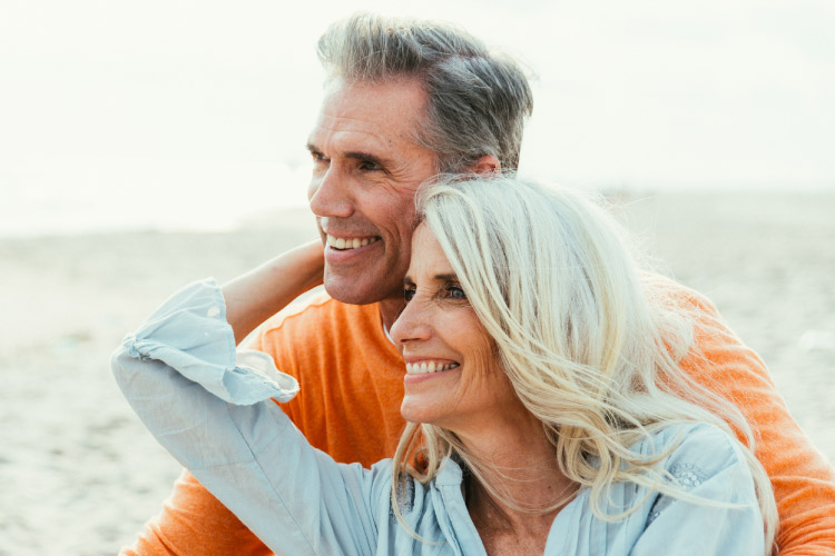 Older couple embraces and smiles by the ocean